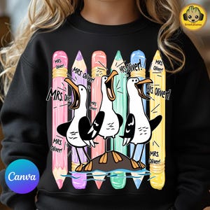 May include: A black sweatshirt featuring a graphic of three white seagulls with black wings standing on a rock, surrounded by five colorful pencils in pink, purple, peach, teal, and yellow. The text "MRS. Oliver!" is repeated multiple times.