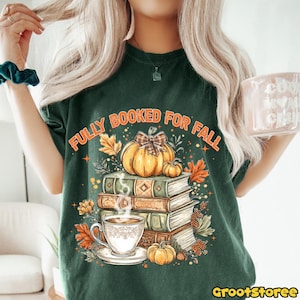 May include: Dark green t-shirt with the text "FULLY BOOKED FOR FALL" above a graphic of pumpkins, books, and a cup of coffee. The design features autumn leaves and a bow. The shirt has a crew neck and short sleeves.