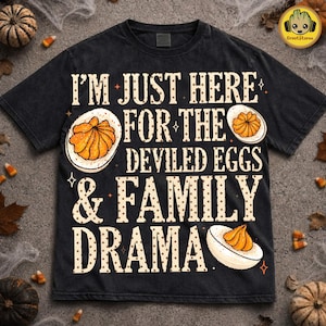 May include: A black short-sleeve t-shirt featuring the text I'M JUST HERE FOR THE DEVILED EGGS & FAMILY DRAMA in a beige dotted font. The design includes illustrations of three halved deviled eggs with orange yolks and white whites.