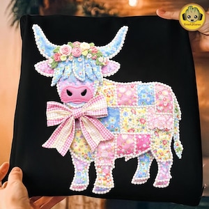 May include: A black pillow featuring a colorful patchwork cow design. The cow has blue horns, a pink nose, and a floral crown. A large pink and white bow is at the neck. The cow's body is made of floral patchwork squares.