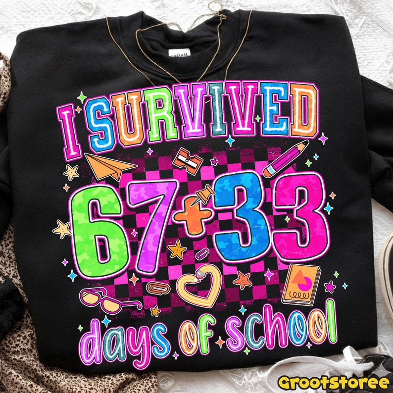May include: Black sweatshirt with the text "I Survived 67 + 33 days of school" in colorful, outlined letters. The design includes a checkered background, stars, and school-themed graphics like a pencil and paper airplane.