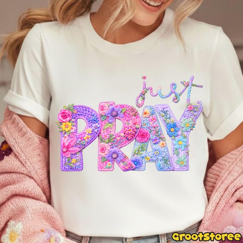 May include: White t-shirt with the words "just PRAY" in a floral design. The word "PRAY" is in large, colorful letters filled with flowers. The word "just" is in cursive above the word "PRAY".