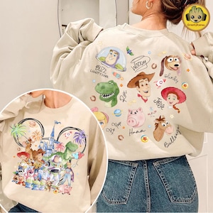 以下が含まれることがあります： ベージュ色のスウェットシャツ。ディズニーのトイ・ストーリーのキャラクターがカラフルにプリントされています。バズ・ライトイヤー、ウッディ、レックス、スリンキーなどがデザインされています。クルーネックと長袖です。