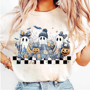 K&ouml;nnte beinhalten: Cremefarbenes Sweatshirt mit einem Halloween-Motiv von drei Cartoon-Geistern. Die Geister sind in Patchwork- und floral gemusterte T&uuml;cher geh&uuml;llt und halten K&uuml;rbislaternen und eine Kaffeetasse. Flederm&auml;use, Sterne und Spinnweben vervollst&auml;ndigen das Design.