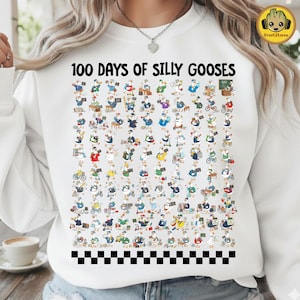 以下が含まれることがあります： 「100 Days of Silly Gooses」の文字と、様々なポーズの漫画のガチョウが描かれた白いスウェットシャツ。ガチョウは様々な衣装とアクティビティで描かれています。下部には白と黒のチェック柄のボーダーがあります。
