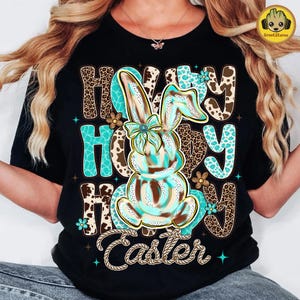 May include: Black t-shirt with a colorful Easter design. The design features a bunny with turquoise and brown accents, the words "Happy Easter" and a rope-style font. The letters have a leopard print pattern.