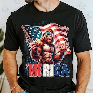 May include: Black t-shirt featuring a muscular Bigfoot character wearing American flag sunglasses and holding a flag. The flag has stars and stripes. The word "'MERICA" is printed in red, white, and blue.