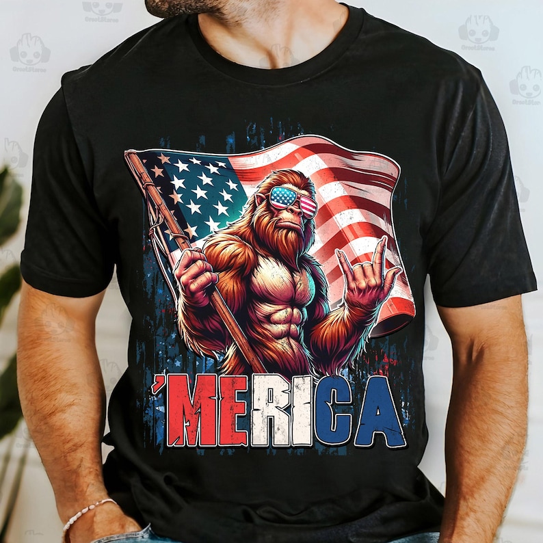 May include: Black t-shirt featuring a muscular Bigfoot character wearing American flag sunglasses and holding a flag. The flag has stars and stripes. The word "'MERICA" is printed in red, white, and blue.