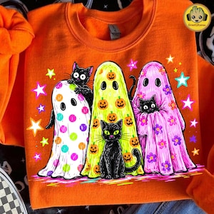 May include: An orange crewneck sweatshirt featuring a graphic print of three ghosts and three black cats. One ghost is white with colorful polka dots, one is yellow with orange pumpkins, and one is pink with purple flowers, surrounded by stars.
