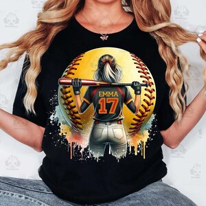 Może przedstawiać: Czarny T-shirt z akwarelowym wzorem przedstawiającym gracza w softbol trzymającego kij. Gracz ma na sobie czarną i czerwoną koszulkę z imieniem "Emma" i numerem "17" na plecach. Piłka do softbolu jest ż&oacute;łta z czerwonymi szwami.