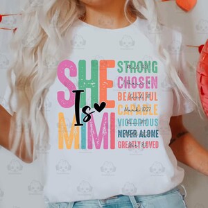 K&ouml;nnte beinhalten: Ein wei&szlig;es T-Shirt mit einer bunten Grafik, auf der "She is Mimi" steht, sowie Bibelverse und W&ouml;rter wie "Stark", "Auserw&auml;hlt", "Sch&ouml;n", "F&auml;hig", "Siegreich", "Niemals allein" und "Sehr geliebt".