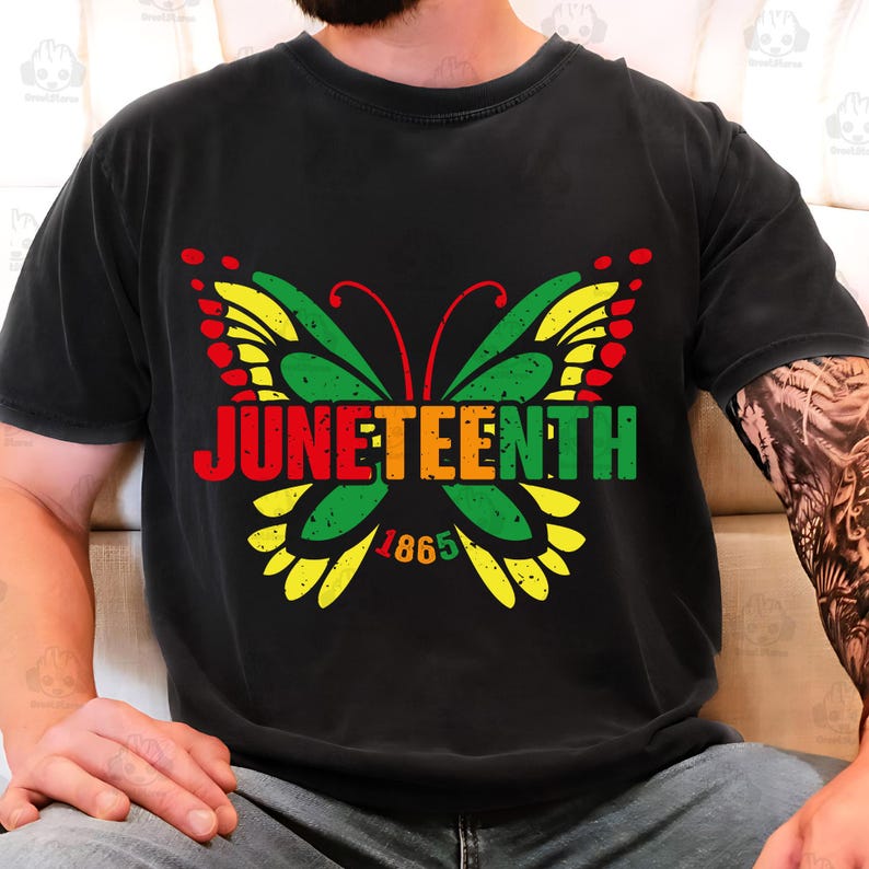 May include: Black t-shirt featuring a colorful butterfly design with the word "Juneteenth" in red, orange, green, and yellow. The year "1865" is below the butterfly. The shirt is a comfortable, casual style.