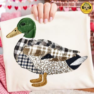 Könnte beinhalten: Ein cremefarbener Stoff mit einem aufgenähten Entenmuster. Die Ente hat einen grünen Kopf, einen beigen Schnabel und einen Körper aus verschiedenen gemusterten Stoffen in Schwarz-, Weiß-, Braun- und Grautönen. Die Entenfüße sind beige. Das GrootStore-Logo befindet sich in der oberen rechten Ecke.