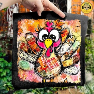 May include: A black square pillow featuring a colorful, whimsical turkey design. The turkey has a pink head, large eyes, and patchwork-style feathers in various patterns and colors. Autumn leaves are scattered around the turkey.