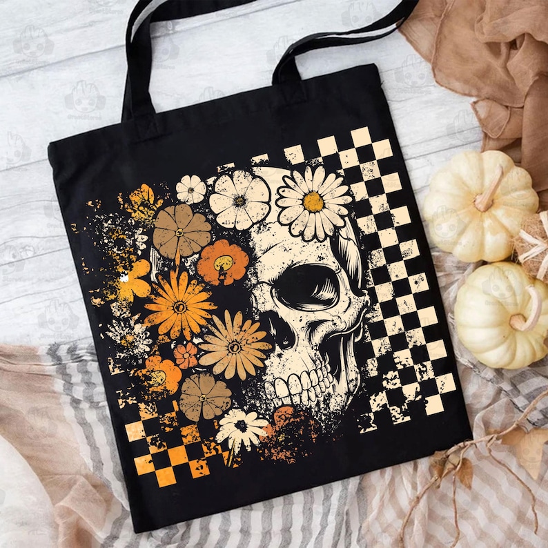 May include: Black tote bag featuring a skull design with floral accents in shades of orange, brown, and cream. The design includes a checkered pattern and a grunge aesthetic. The bag has black handles.