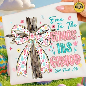 May include: White t-shirt with a wooden cross and a floral bow. The text reads "Even In The Chaos His Grace Still Finds Me" in pink and teal. The design includes Easter eggs and flowers, perfect for the spring season.