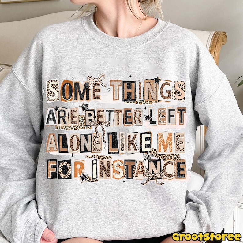 Puede incluir: Sudadera gris claro con el texto "SOME THINGS ARE BETTER LEFT ALONE LIKE ME FOR INSTANCE". El texto est&aacute; en un estilo collage con estampado de leopardo y lazos.