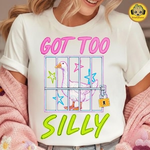 K&ouml;nnte beinhalten: Wei&szlig;es T-Shirt mit einer Grafik einer Gans in einem K&auml;fig, mit den Worten "GOT TOO SILLY" in Pink und Gr&uuml;n. Die Gans ist wei&szlig; mit orangefarbenem Schnabel und F&uuml;&szlig;en, und der K&auml;fig hat blaue und rosa Sterne.