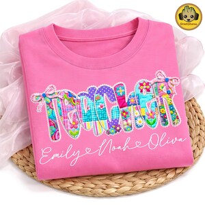 Pode incluir: Uma camiseta rosa com a palavra "TEACHER" em letras de patchwork coloridas. As letras são decoradas com flores e tecidos estampados. Abaixo da palavra estão os nomes "Emily", "Noah" e "Olivia" em escrita branca.