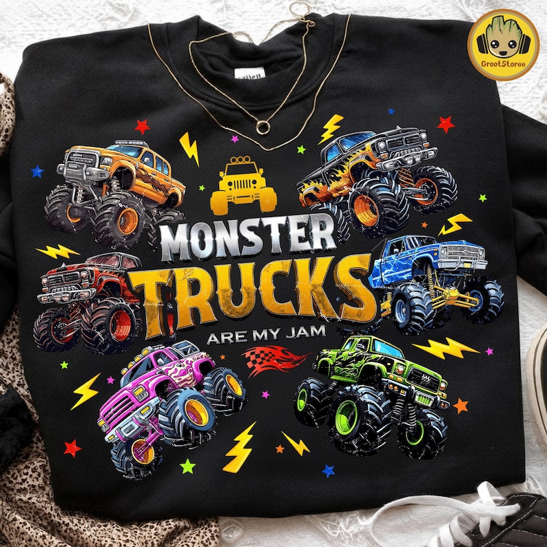 May include: Black sweatshirt featuring a colorful graphic of several monster trucks with large tires. The text "MONSTER TRUCKS ARE MY JAM" is prominently displayed. Lightning bolts and stars surround the trucks, creating a dynamic design.