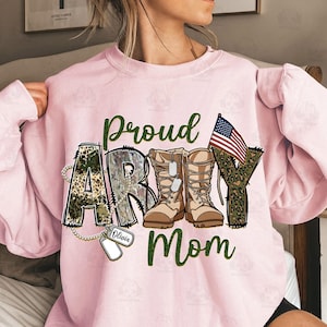 May include: Pink sweatshirt with a camouflage and leopard print design that says "Proud Army Mom" with a pair of brown boots and an American flag. The word "Olivia" is written on a dog tag.