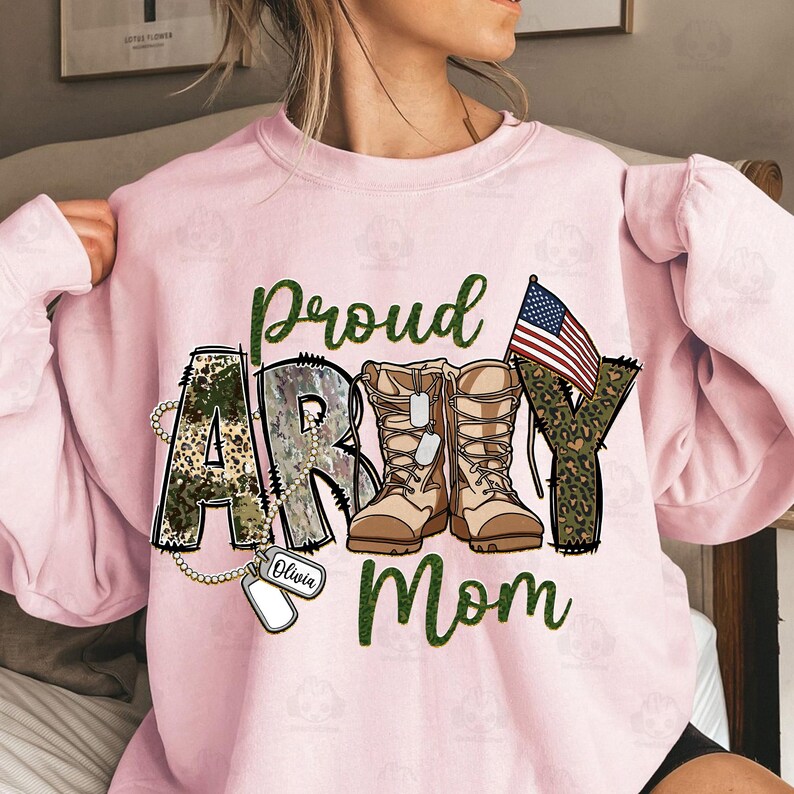May include: Pink sweatshirt with a camouflage and leopard print design that says "Proud Army Mom" with a pair of brown boots and an American flag. The word "Olivia" is written on a dog tag.