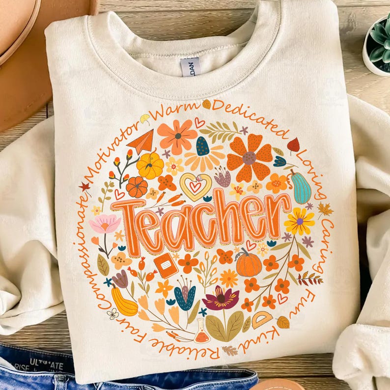 May include: Cream-colored sweatshirt with a floral design and the word "Teacher" in orange. The design includes flowers, pumpkins, and the words "Motivator," "Warm," "Dedicated," "Loving," "Caring," "Fun," "Kind," "Reliable," and "Fair."