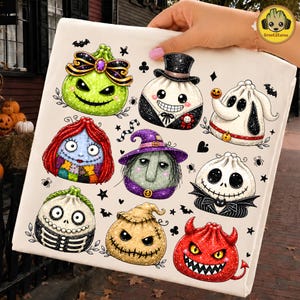 May include: A white fabric item featuring a colorful graphic print of nine stylized, round, dumpling-shaped characters inspired by Halloween themes, including a green pumpkin, a skeleton, a witch, a devil, and various spooky figures.