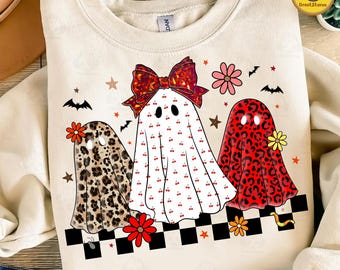 May include: Cream-colored sweatshirt featuring three ghost characters with unique patterns and accessories. One ghost has a leopard print, another is white with cherry accents, and the third has a red leopard print. The design includes flowers, stars, bats, and a checkered border.