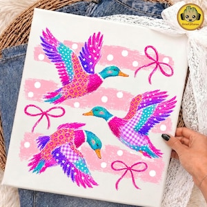 Könnte beinhalten: Ein weißer Leinwanddruck mit drei fliegenden Enten in leuchtenden Rosa-, Blau- und Violetttönen. Die Enten haben gemusterte Flügel mit Sternen, Punkten und Vichy-Karos. Drei rosa Schleifen und weiße Punkte verzieren den Hintergrund.