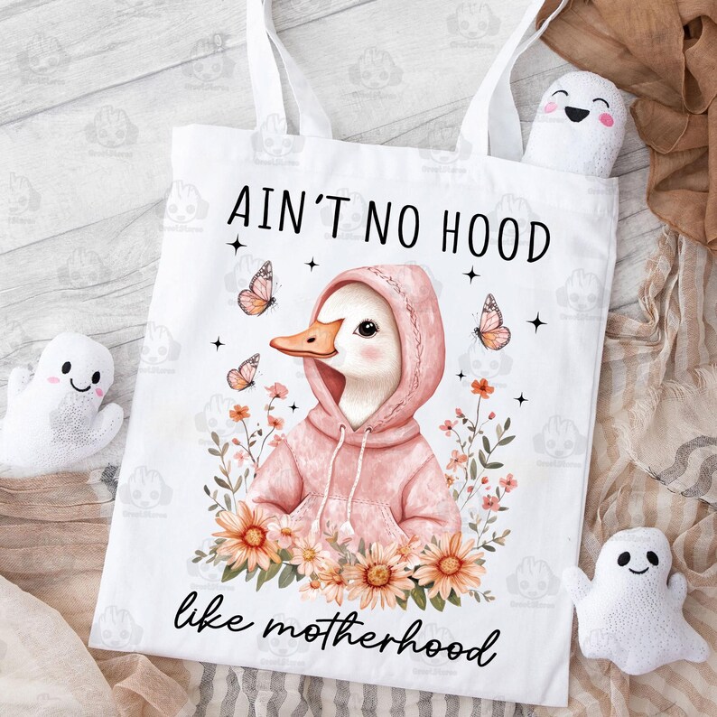 May include: White tote bag with a pink duck wearing a pink hoodie and surrounded by flowers. The text on the bag reads "Ain't no hood like motherhood".