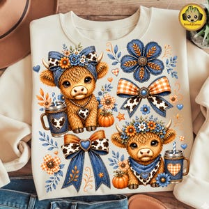 May include: A cream-colored sweatshirt featuring a graphic print of two fluffy highland calves. One calf wears a blue floral bow, the other a floral crown. The design includes blue and orange plaid bows, pumpkins, and mugs with heart patterns.