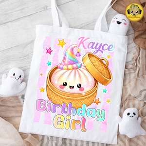 May include: A white tote bag featuring a graphic of a cute, smiling steamed bun in a bamboo steamer basket, wearing a colourful party hat. The text reads Kayce Birthday Girl in pastel colours, surrounded by small stars and pink vertical stripes.