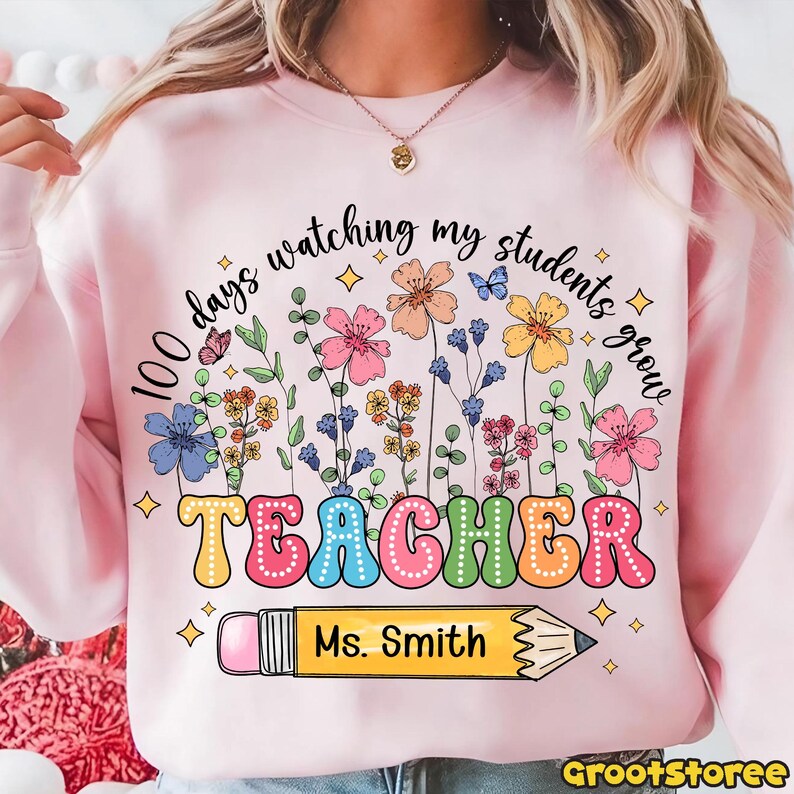 May include: Pink sweatshirt with a colorful floral design and the text "100 days watching my students grow TEACHER Ms. Smith" with a pencil graphic. The design includes butterflies and stars.