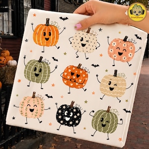 May include: A white fabric sheet featuring a repeating pattern of nine cartoon pumpkins with faces, arms, and legs. The pumpkins vary in color and design, including orange, cream, pink, green, and black, accented by small stars and black bats.