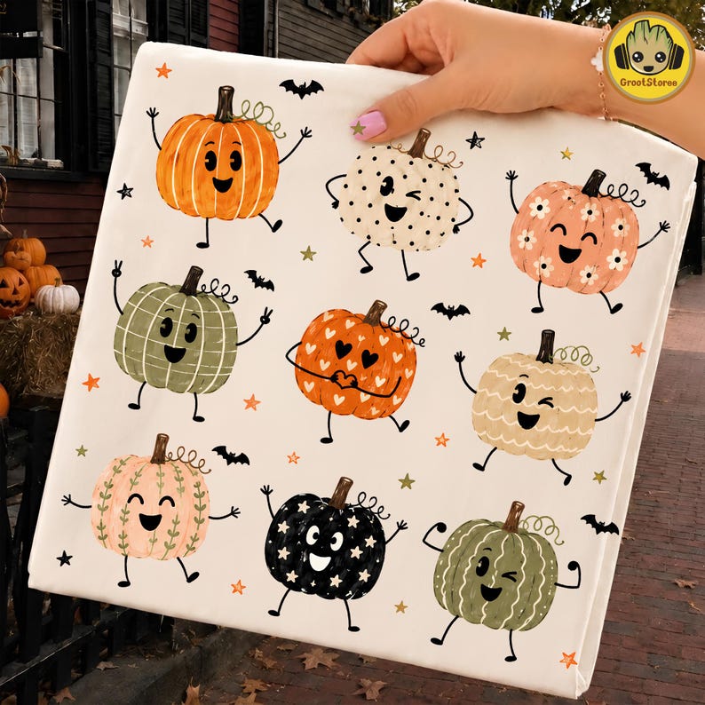 May include: A white fabric sheet featuring a repeating pattern of nine cartoon pumpkins with faces, arms, and legs. The pumpkins vary in color and design, including orange, cream, pink, green, and black, accented by small stars and black bats.