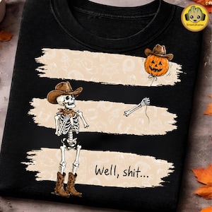 Könnte beinhalten: Ein schwarzes T-Shirt mit einer Grafik eines Skeletts, das einen Cowboyhut und Stiefel trägt und eine Schnur zu einem Kürbis mit Cowboyhut hält. Das Design umfasst drei beige Pinselstrich-Bänder mit Western-Mustern und den Text Well, shit...