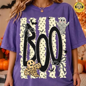 May include: A purple short-sleeve t-shirt featuring a large black graphic that spells BOO. The design includes a leopard print ghost, a checkered ghost, black bows, and small bat silhouettes over a cream-colored background with polka dots.