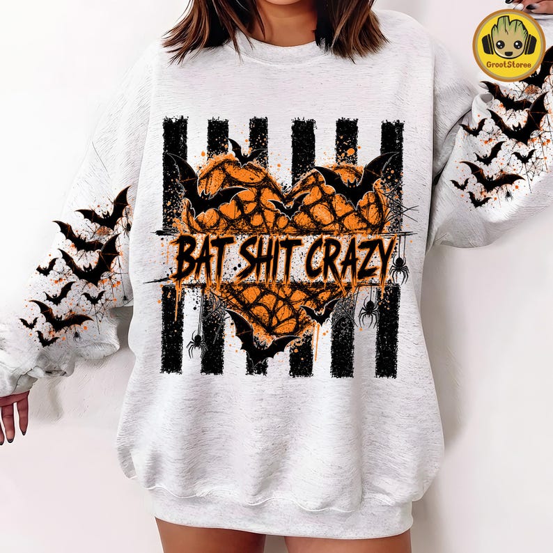 May include: A light gray crewneck sweatshirt featuring a central graphic of an orange heart made of spiderwebs, overlaid with black bats and the text BAT SHIT CRAZY. Vertical black stripes run behind the heart, and bats decorate both sleeves.