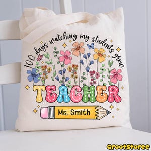 May include: Cream-colored tote bag with a colorful floral design and the words "100 days watching my students grow TEACHER Ms. Smith" printed on it. A pencil graphic is also included.
