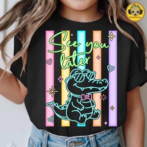 May include: Black t-shirt with a colorful design featuring a cartoon alligator wearing sunglasses and a bow tie. The text "See you later" is written above the alligator, with vertical stripes in the background.
