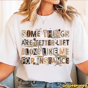 Puede incluir: Camiseta blanca con el texto "SOME THINGS ARE BETTER LEFT ALONE LIKE ME FOR INSTANCE" en una mezcla de letras de leopardo, marr&oacute;n y negro. El dise&ntilde;o incluye estrellas y lazos.