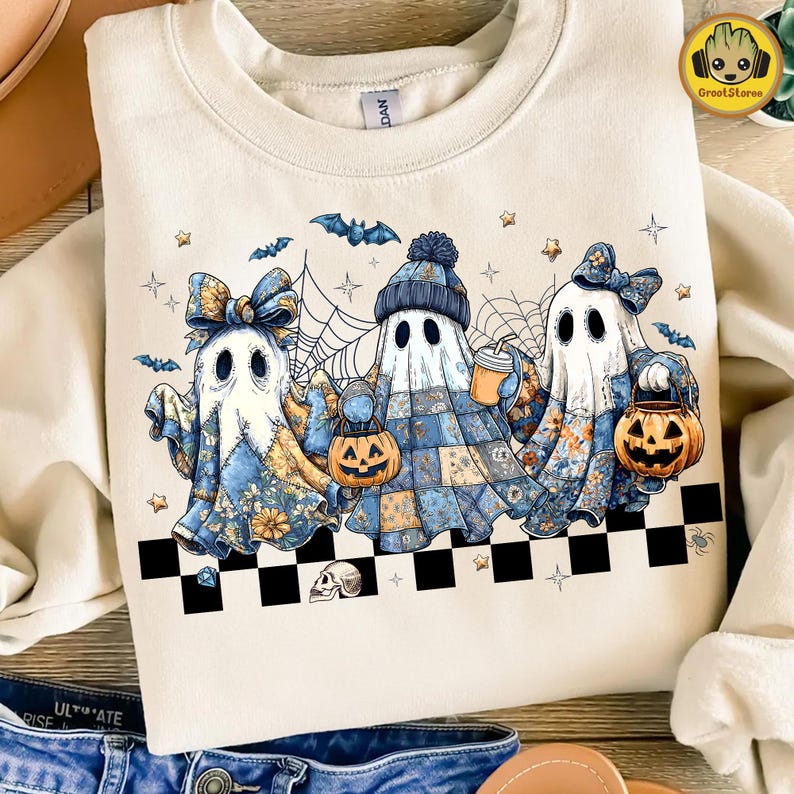 K&ouml;nnte beinhalten: Cremefarbenes Sweatshirt mit einem Halloween-Motiv. Die Grafik zeigt drei Geisterfiguren in Patchwork-Outfits, die K&uuml;rbislaternen und Getr&auml;nke halten. Flederm&auml;use, Sterne und Spinnweben erg&auml;nzen das Design. Unten befindet sich ein schwarz-wei&szlig;es Schachbrettmuster.