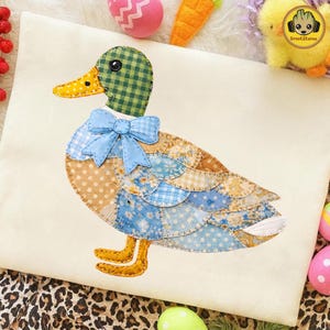 May include: A decorative duck applique with a patchwork design. The duck features a green checkered head, a yellow dotted beak, and a blue bow. The body is made of various patterned fabrics, including polka dots and floral prints. The applique is on a cream-colored background.