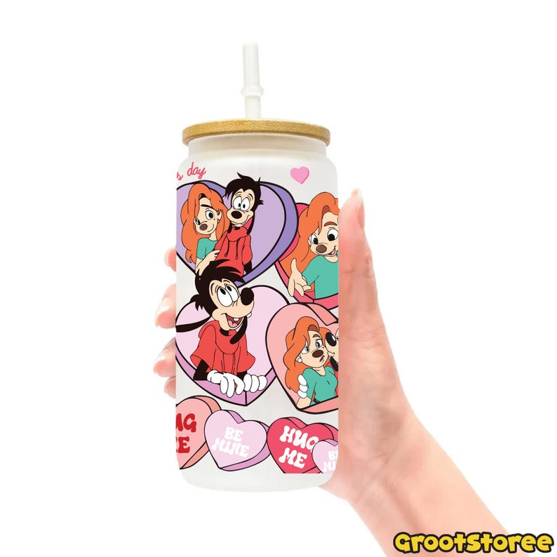 May include: A white glass can-shaped tumbler with a bamboo lid and a white straw. The tumbler features cartoon characters in heart-shaped designs and candy hearts with text. The tumbler is held by a hand.