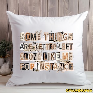 Puede incluir: Coj&iacute;n cuadrado blanco con el texto "SOME THINGS ARE BETTER LEFT ALONE LIKE ME FOR INSTANCE" en una mezcla de fuentes y patrones, incluyendo estampado de leopardo y estrellas. El coj&iacute;n tiene lazos decorativos.