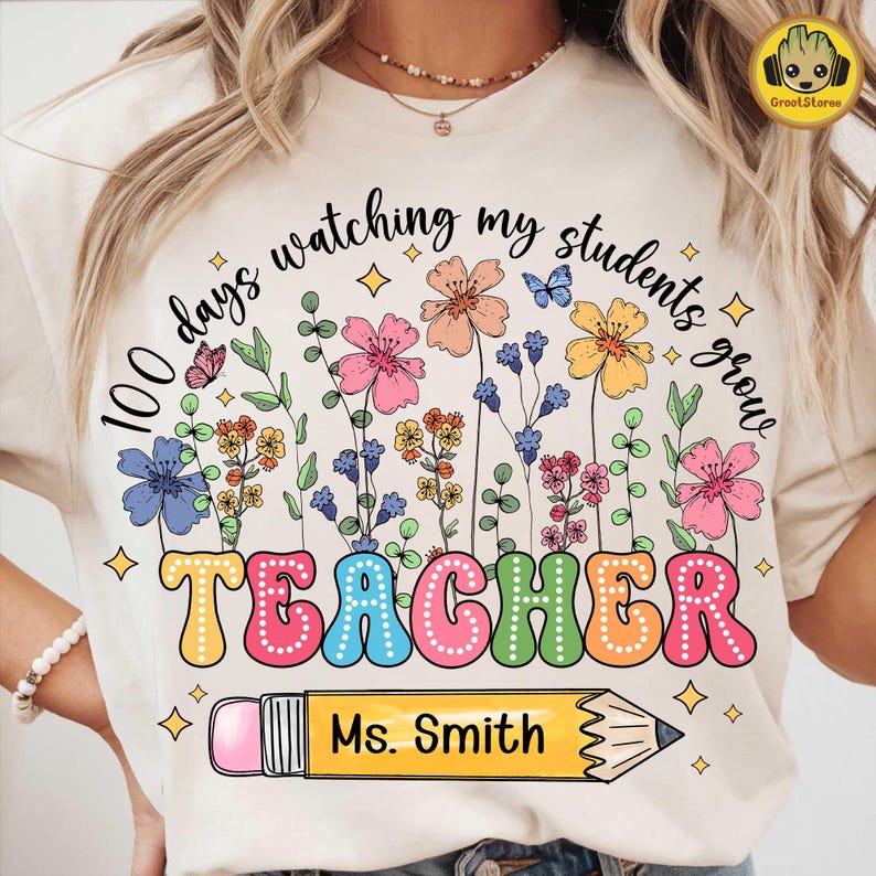 May include: Cream-colored t-shirt with a colorful floral design and the words "100 days watching my students grow TEACHER Ms. Smith" in a playful font. A yellow pencil graphic is below the word TEACHER.