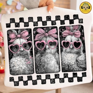 May include: A white decorative pillow featuring three chick illustrations wearing pink heart-shaped sunglasses and bows. The chicks are set against a black background with floral accents. The pillow has a black and white checkered border.