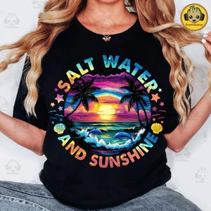 May include: Black t-shirt with a colorful graphic of a sunset over the ocean with palm trees, dolphins, and seashells. The text "Salt Water and Sunshine" is written in a rainbow arc around the graphic.