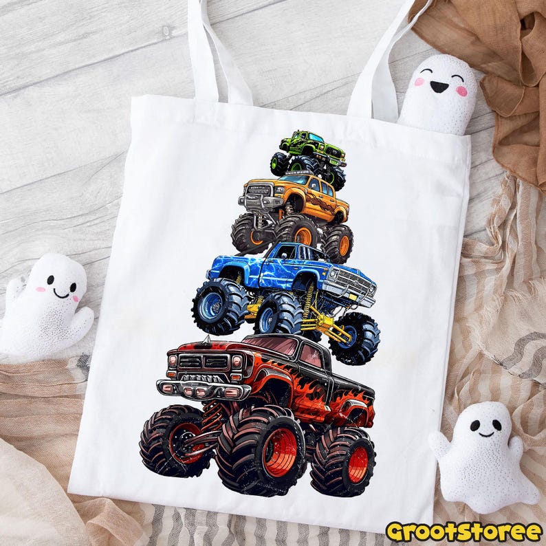 May include: White tote bag featuring a stack of five colorful monster trucks. The trucks are red, blue, orange, green, and black, with large tires and detailed graphics. The bag has two white handles and the text "GrootStoree" at the bottom.
